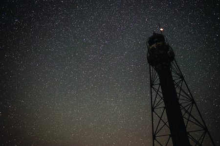 Silhouettes of the Old Lighthouse sandy beach and ocean against the background of the starry skyの写真素材