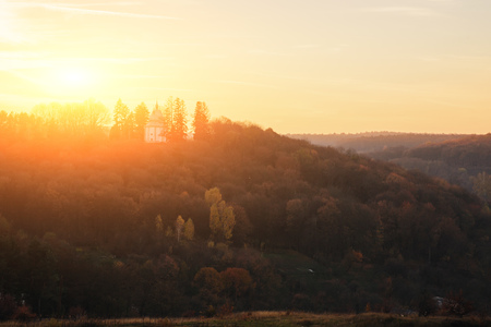 Landscape of old solitary church on the hill with autumn forest during the sunset .の写真素材