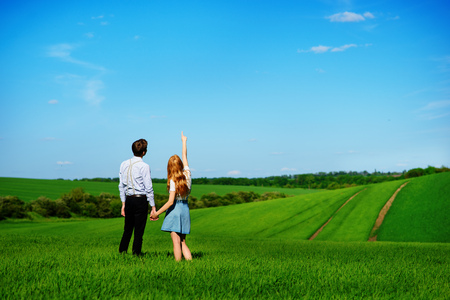 A young couple standing in the field, the girl shows her hand to the sky.の写真素材
