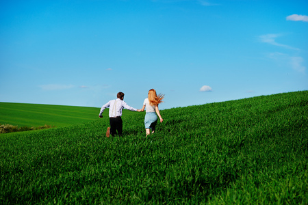 Young happy lovers running on meadow with green grass and blue sky, From the back.の写真素材