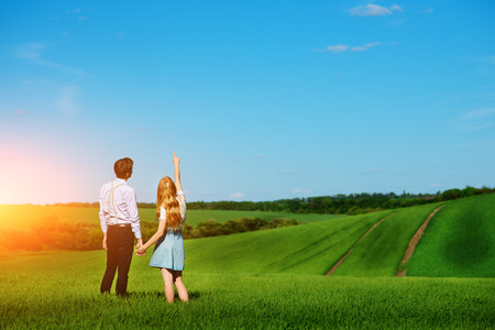 A young couple standing in the field, the girl shows her hand to the sky.の写真素材