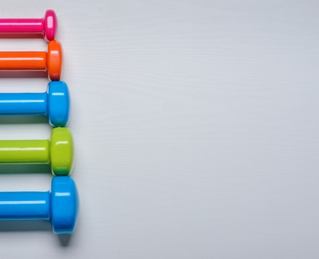 many blue green and one orange in the middle dumbbells on a white background ,concept preparing to fitness sports equipment top view mock up.の写真素材