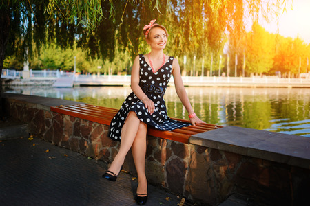 A beautiful young woman dressed sits on a bench near the pond.の写真素材