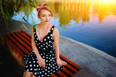 A beautiful young woman dressed sits on a bench near the pond.の写真素材