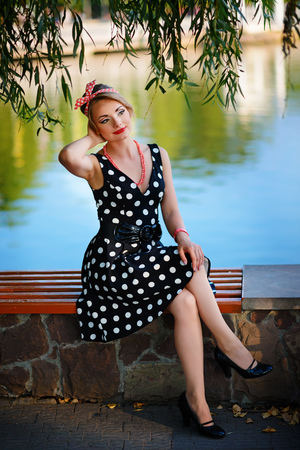 A beautiful young woman dressed sits on a bench near the pond.の写真素材