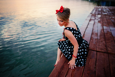 A beautiful young woman dressed sitting on the pier.の写真素材