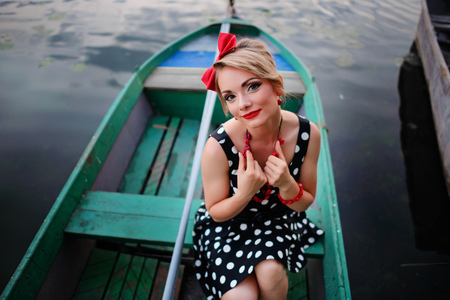 Beautiful young woman dressed dressed in a boat on a lake shore.の写真素材
