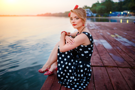 A beautiful young woman dressed sitting on the pier.の写真素材