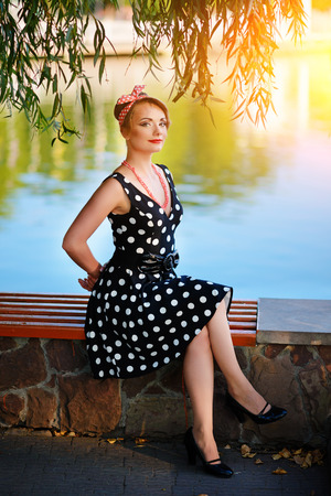 A beautiful young woman dressed sits on a bench near the pond.の写真素材
