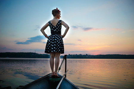 A beautiful young woman dressed standing by the lake, on the background of the sunset.の写真素材