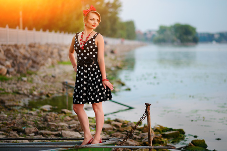 A beautiful young woman dressed standing by the lake, on the background of the sunset.の写真素材