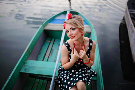 Beautiful young woman dressed dressed in a boat on a lake shore.の写真素材