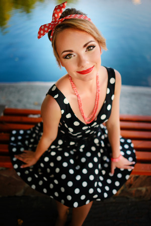 A beautiful young woman dressed sits on a bench near the pond.の写真素材