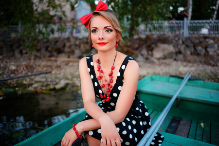 Beautiful young woman dressed dressed in a boat on a lake shore.の写真素材