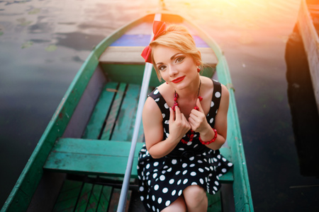 Beautiful young woman dressed dressed in a boat on a lake shore.の写真素材