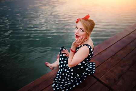 A beautiful young woman dressed sitting on the pier.の写真素材