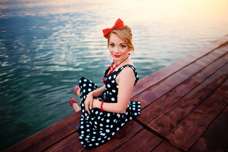 A beautiful young woman dressed sitting on the pier.の写真素材