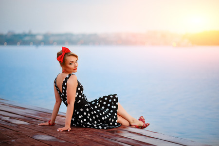 A beautiful young woman dressed sitting on the pier.の写真素材