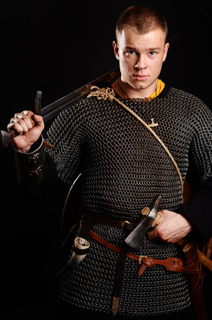 A soldier in a chain of letters stands with a sword in his hands on a black background.の写真素材