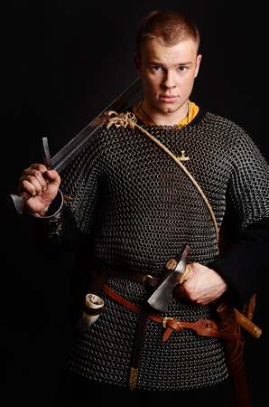 A soldier in a chain of letters stands with a sword in his hands on a black background.の写真素材