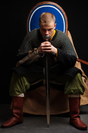 A soldier in a chain of letters is sitting holding a sword in his hands.の写真素材
