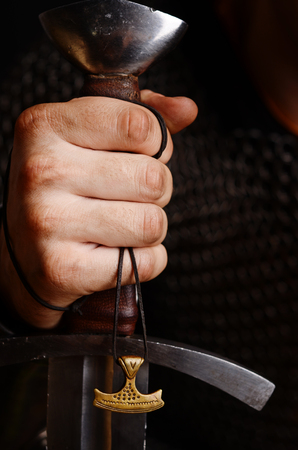 a hand holds a sword, an amulet of a torch hammer hanging on a lace.の写真素材