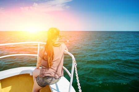 The girl sits on the boat's nose and looks at the ocean.の写真素材