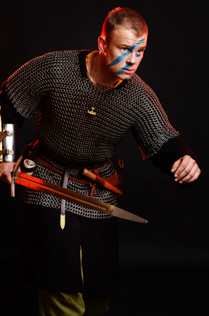 A soldier in a chain of letters stands with a sword in his hands on a black background.の写真素材