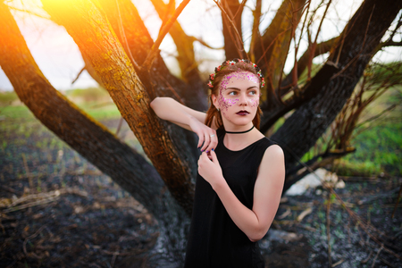 A young beautiful woman with a violet shine on her face stands near a burnt tree.の写真素材