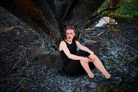 A young beautiful woman with a violet shine on her face stands near a burnt tree.の写真素材