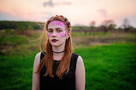 A young beautiful woman with a violet shine on her face standing on the grass and looking at the camera.の写真素材