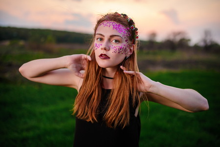 A young beautiful woman with a violet shine on her face standing on the grass and looking at the camera.の写真素材