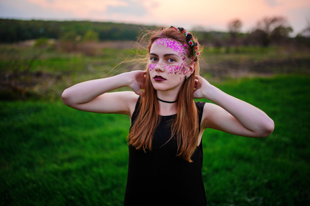 A young beautiful woman with a violet shine on her face standing on the grass and looking at the camera.の写真素材