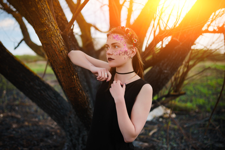 A young beautiful woman with a violet shine on her face stands near a burnt tree.の写真素材