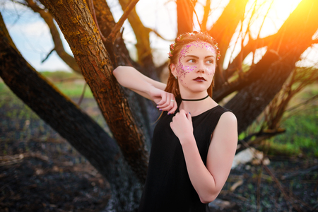 A young beautiful woman with a violet shine on her face stands near a burnt tree.の写真素材
