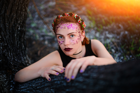 A young beautiful woman with a violet shine on her face sits near a burnt tree.の写真素材