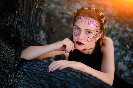A young beautiful woman with a violet shine on her face sits near a burnt tree.の写真素材