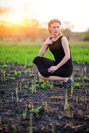 A young beautiful woman with a violet shine on her face stands near a burnt tree.の写真素材