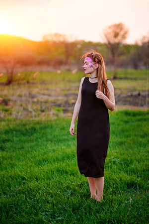 A young beautiful woman with a violet shine on her face stands on the grass.の写真素材