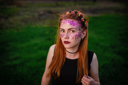 A young beautiful woman with a violet shine on her face standing on the grass and looking at the camera.の写真素材