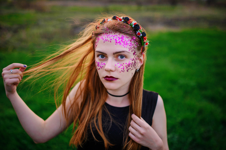 A young beautiful woman with a violet shine on her face standing on the grass and looking at the camera.の写真素材