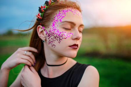 A young beautiful woman with a violet shine on her face standing on the grass and looking right.の写真素材