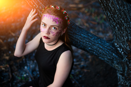 A young beautiful woman with a violet shine on her face stands near a burnt tree.の写真素材