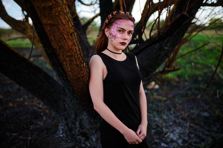 A young beautiful woman with a violet shine on her face stands near a burnt tree.の写真素材