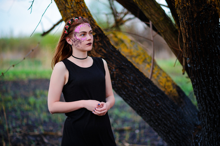 A young beautiful woman with a violet shine on her face stands near a burnt tree.の写真素材