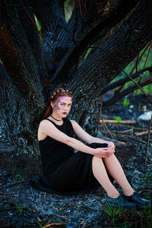 A young beautiful woman with a violet shine on her face stands near a burnt tree.の写真素材