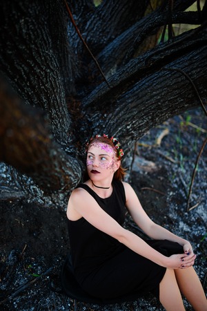 A young beautiful woman with a violet shine on her face stands near a burnt tree.の写真素材