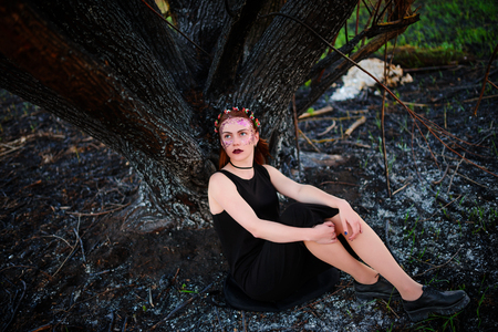 A young beautiful woman with a violet shine on her face stands near a burnt tree.の写真素材