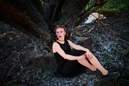 A young beautiful woman with a violet shine on her face stands near a burnt tree.の写真素材