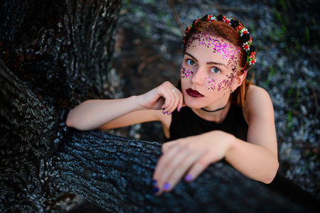 A young beautiful woman with a violet shine on her face sits near a burnt tree.の写真素材